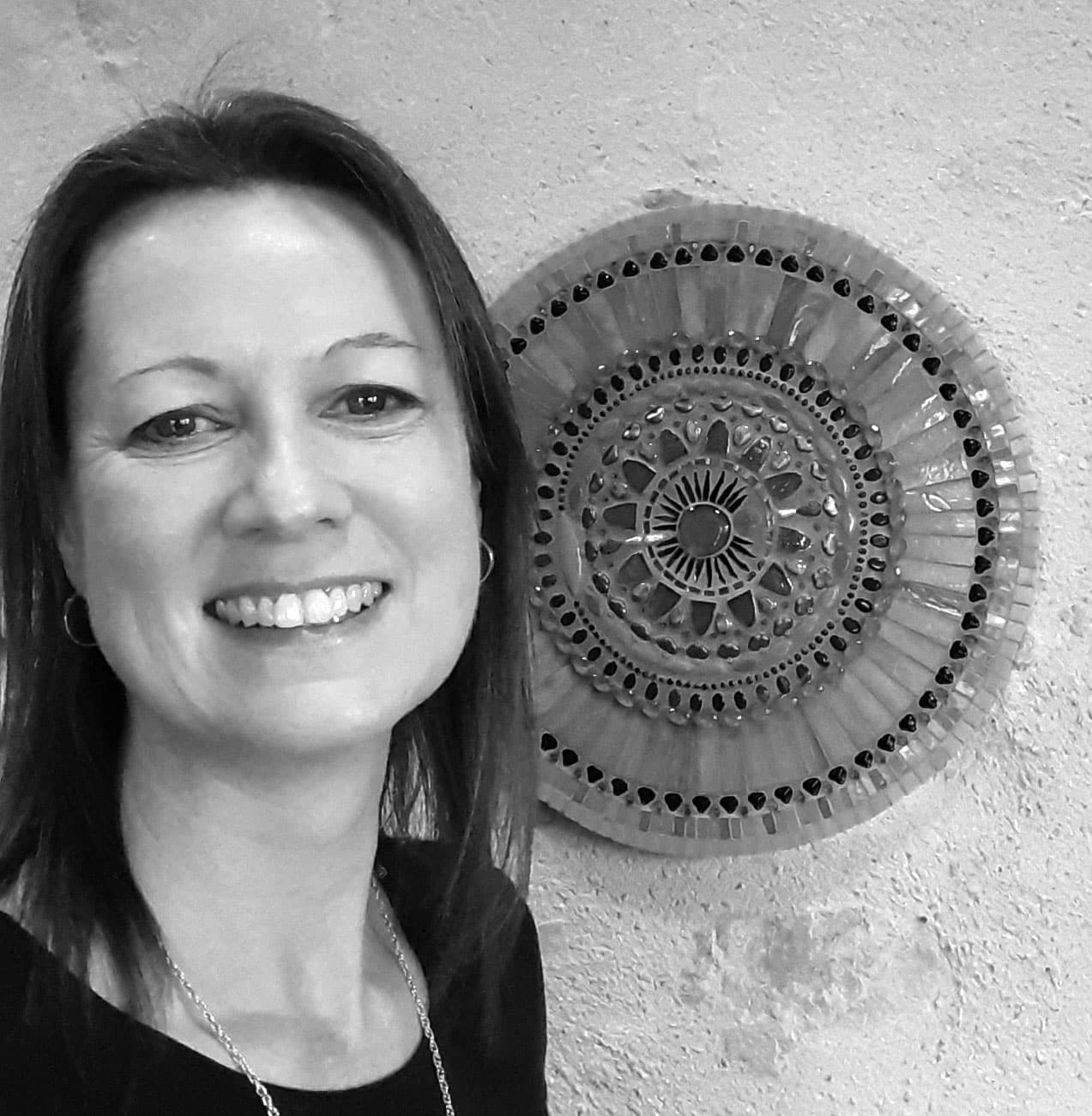Sarah Berry in black and white standing in front of a large mandala hanging on a stone textured wall