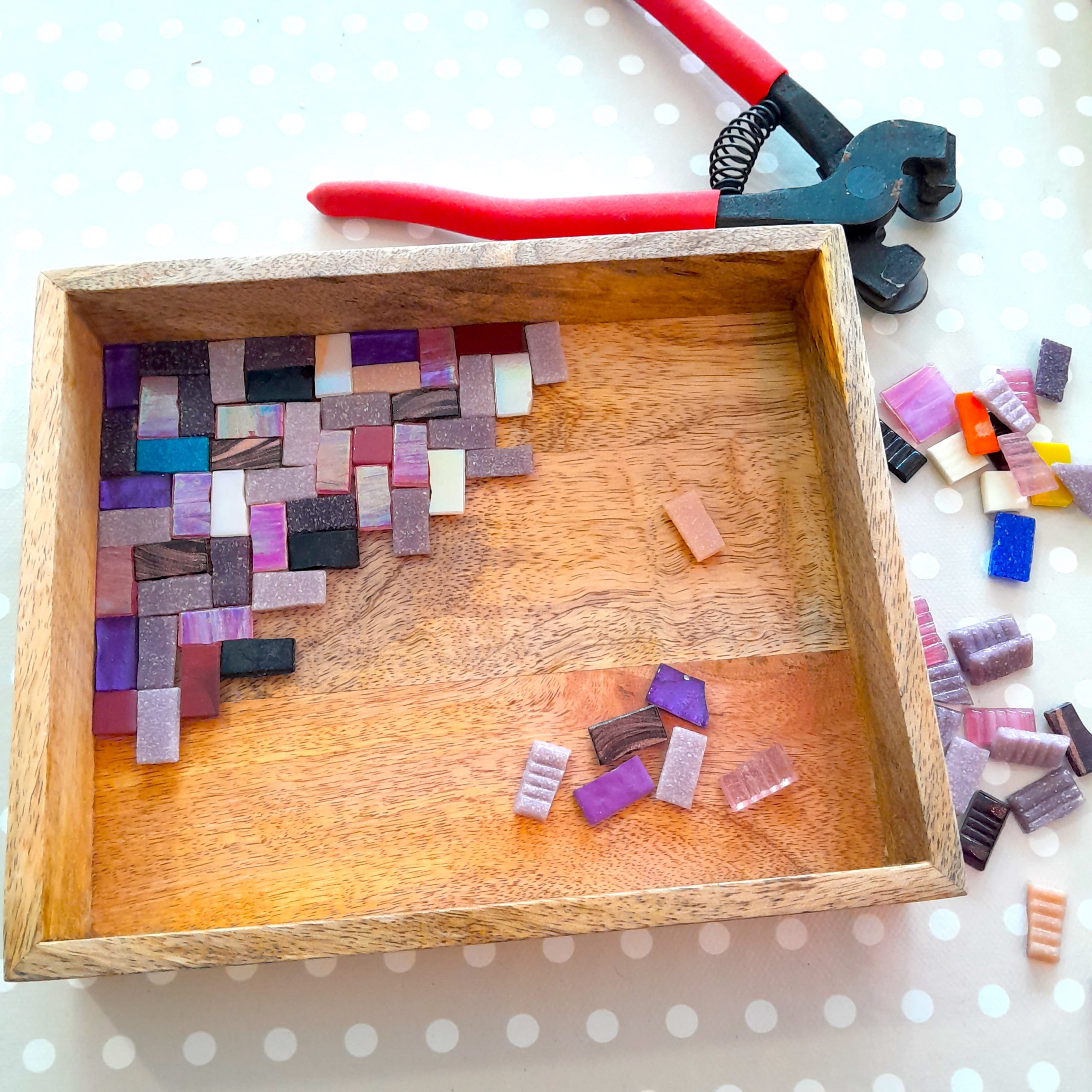 wooden tray sitting on a table with colourful mosaic tile nippers, mosaic tiles around it.